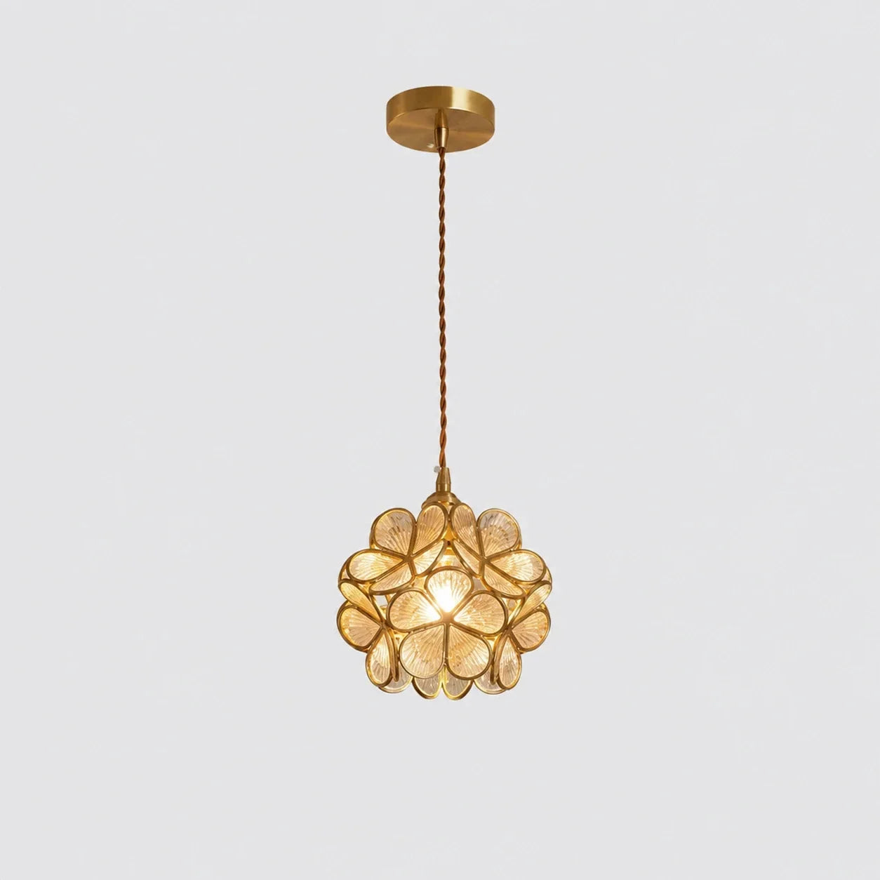 Floral glass petal pendant light with a warm glowing bulb, featuring transparent glass petals and a metallic finish, suspended by a twisted cable.