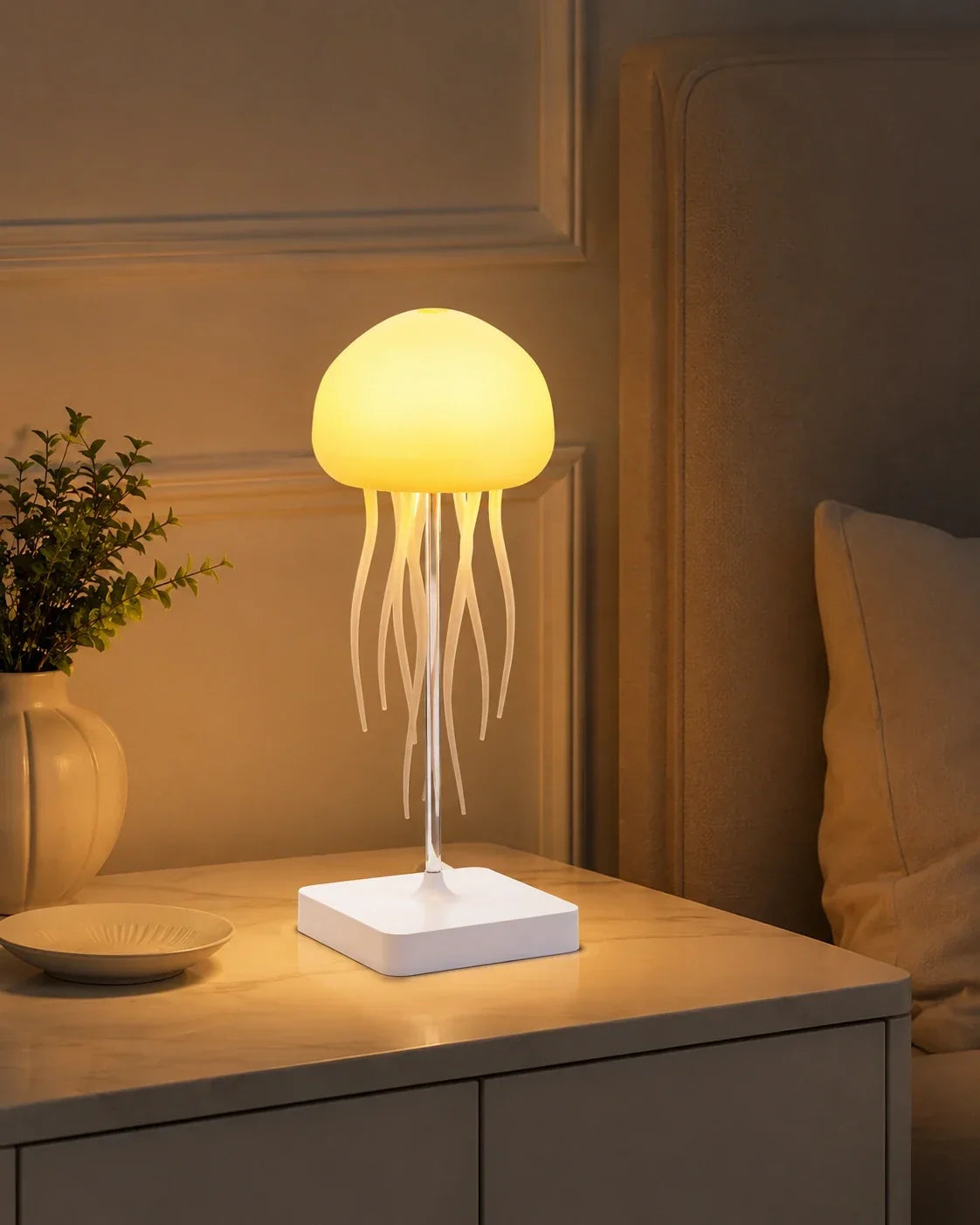 A jellyfish-shaped LED table lamp glowing with a warm yellow light on a bedside table, creating a cosy ambient atmosphere in a bedroom.