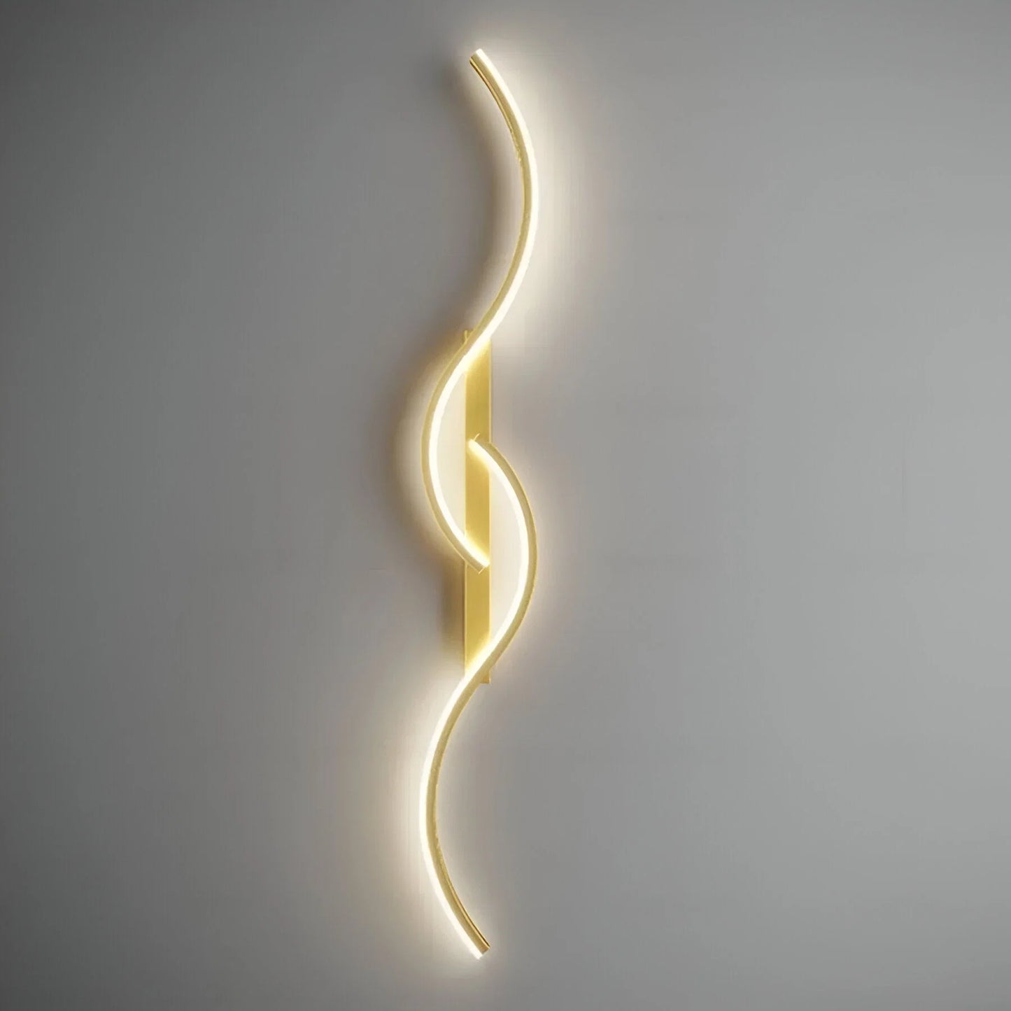 Minimalist gold curved LED wall light with a sleek wave design, mounted vertically on a grey wall and emitting a soft, warm glow for indoor lighting.