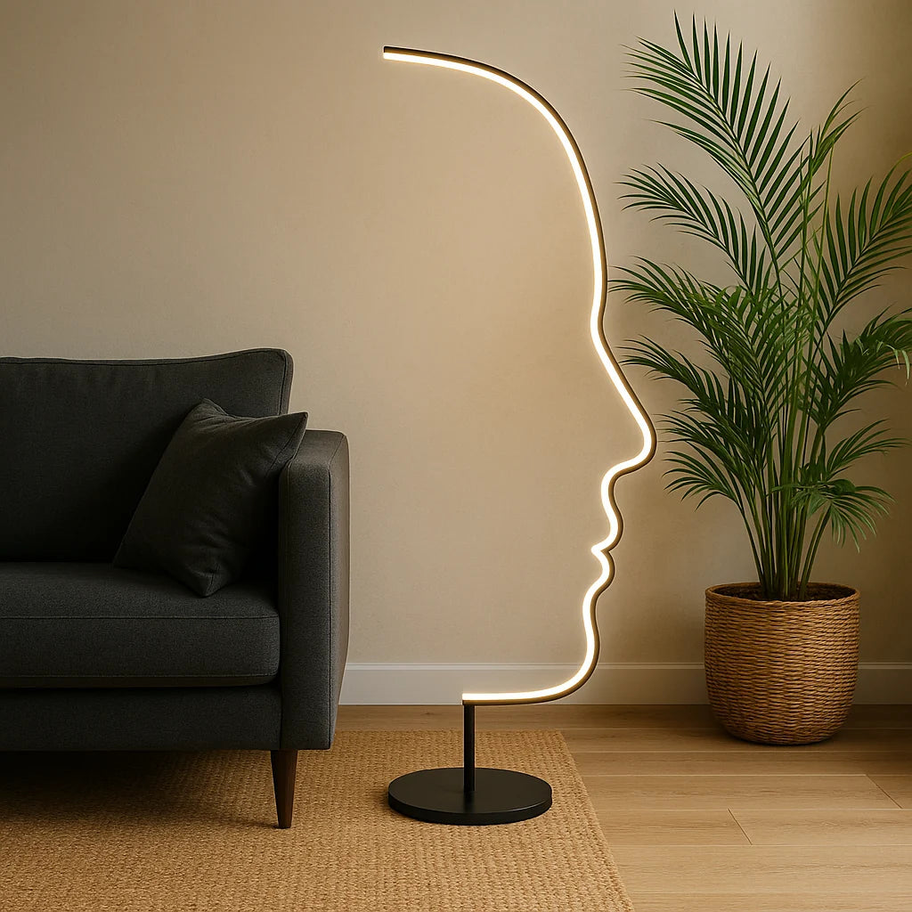 Modern LED floor lamp with an artistic human face outline design, glowing warmly next to a grey sofa and a potted palm in a living room.