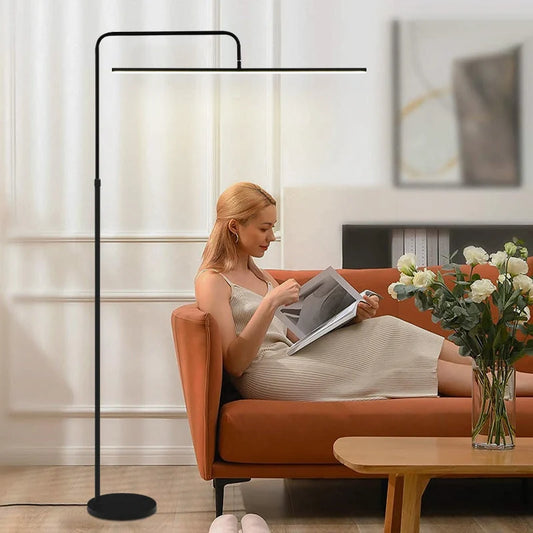 A modern black adjustable LED floor lamp providing bright reading light for a woman sitting on an orange sofa in a living room.