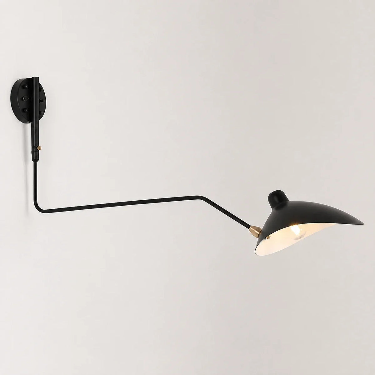 An adjustable black swing-arm wall lamp with a curved metal shade, mounted on a plain white wall and illuminated to cast a warm, inviting glow.