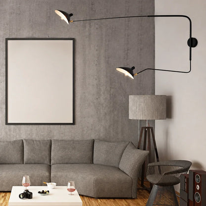 A modern black adjustable swing-arm wall lamp with two lights, mounted in a contemporary living room with a grey sofa and concrete-effect wall.