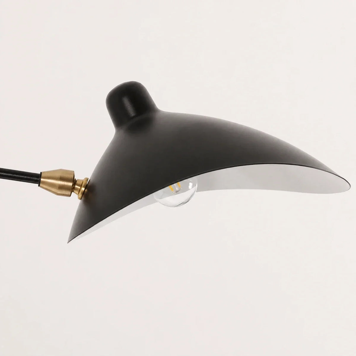 Close-up of the black curved shade of an adjustable swing-arm wall lamp, showing the brass-coloured joint and light bulb against a plain background.