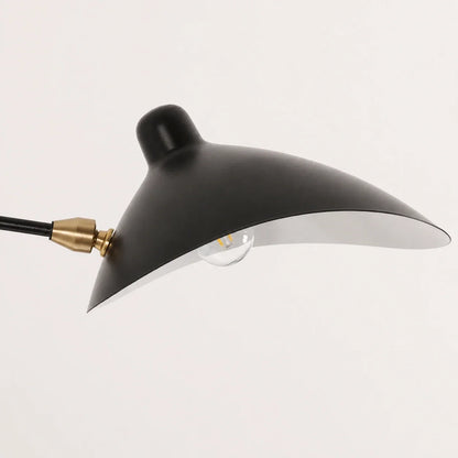 Close-up of the black curved shade of an adjustable swing-arm wall lamp, showing the brass-coloured joint and light bulb against a plain background.
