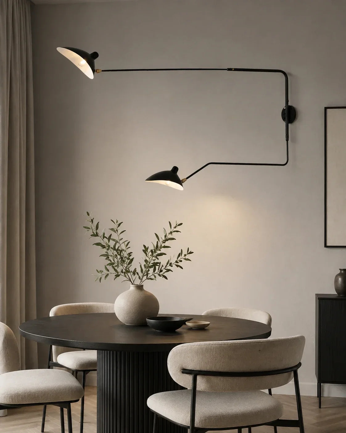 A modern black adjustable swing-arm wall lamp with two lights, mounted on a neutral wall above a contemporary dining table and chairs.