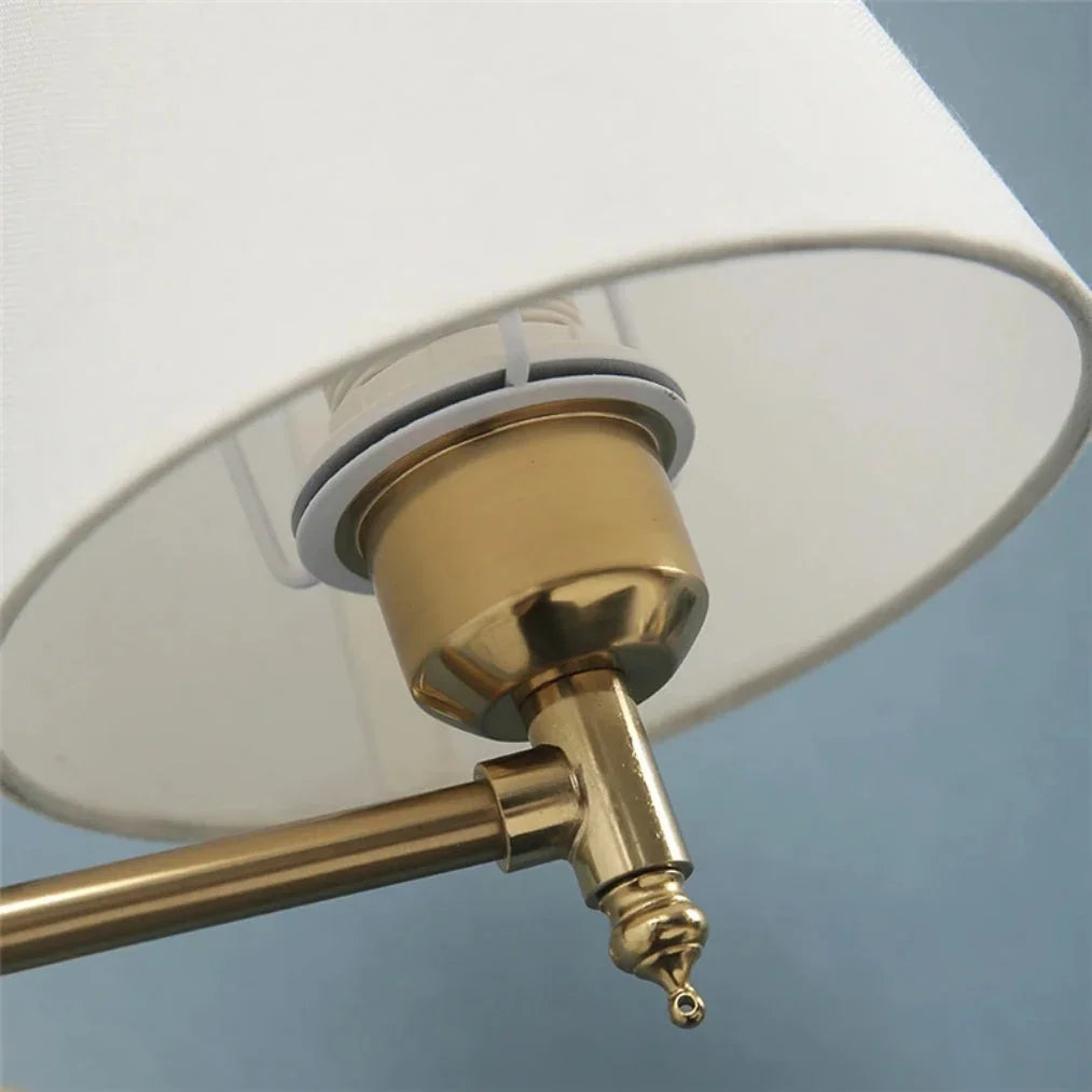 Close-up of the brass-coloured metal fixture and adjustable joint of a swing arm wall lamp, featuring a white fabric shade against a blue wall.