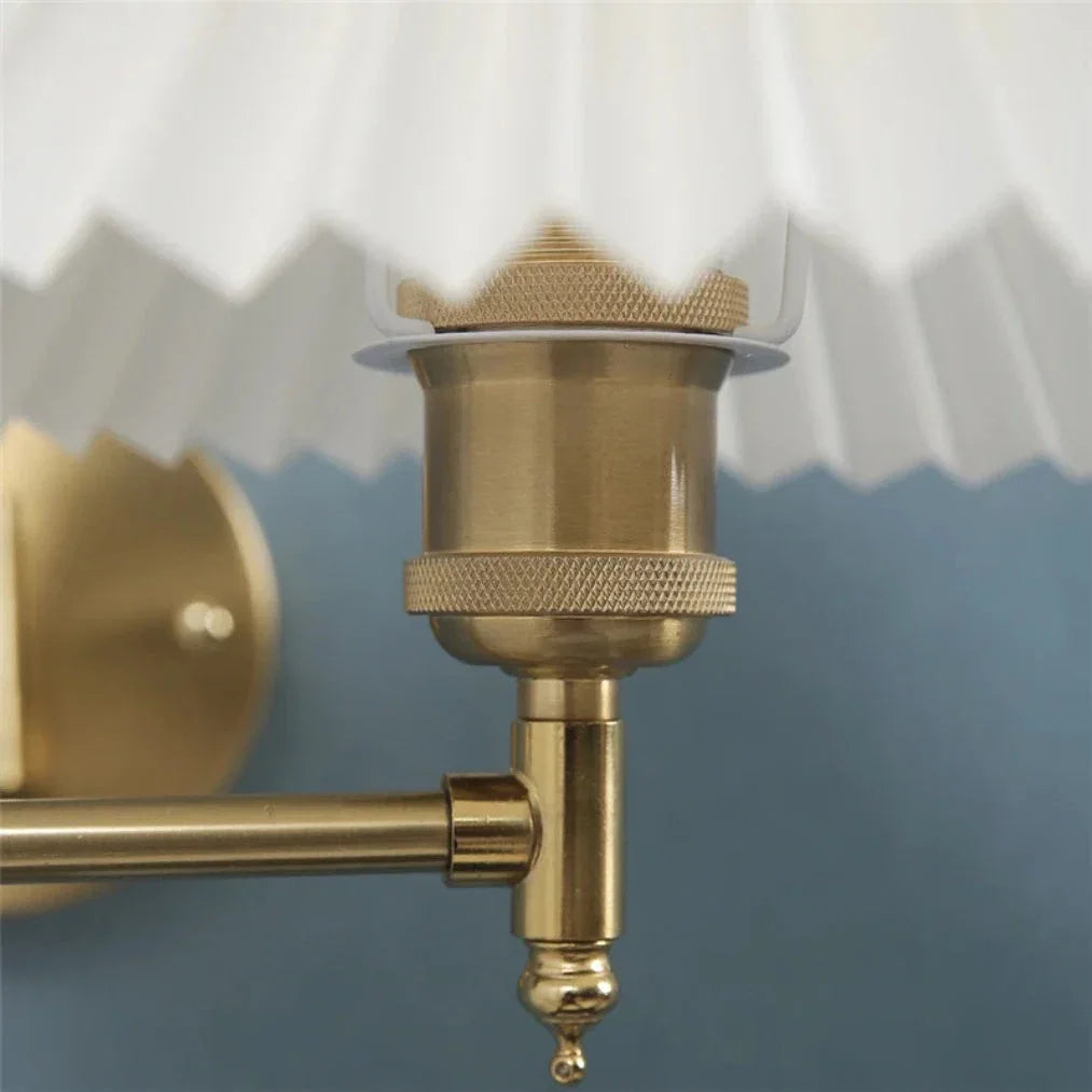 Close-up of the brass-coloured fixture and joint of an adjustable swing arm wall lamp, featuring a white pleated fabric shade against a blue wall.