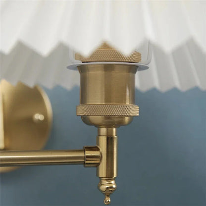 Close-up of the brass-coloured fixture and joint of an adjustable swing arm wall lamp, featuring a white pleated fabric shade against a blue wall.