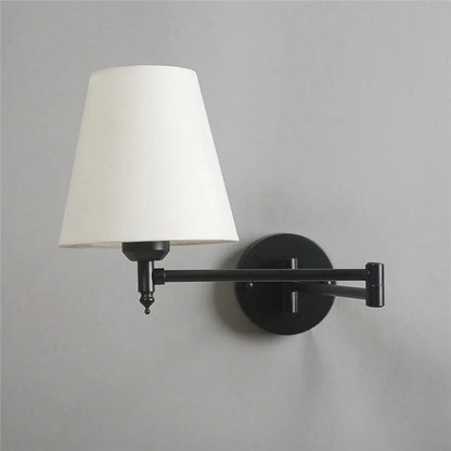Modern adjustable swing arm wall lamp featuring a black metal fixture and a tapered white fabric shade, mounted on a light grey wall.