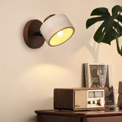 Adjustable travertine and wood wall light illuminated on a neutral wall, casting a warm glow over a vintage radio on a wooden table.