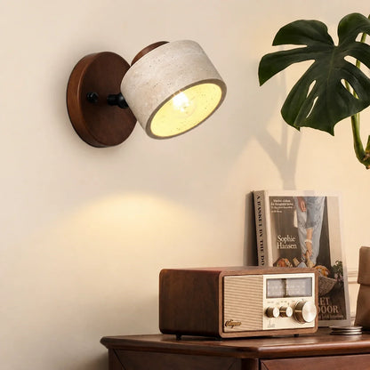 Adjustable wall light featuring a natural travertine stone spotlight head mounted on a dark wood circular base, illuminating a cosy Japandi interior.