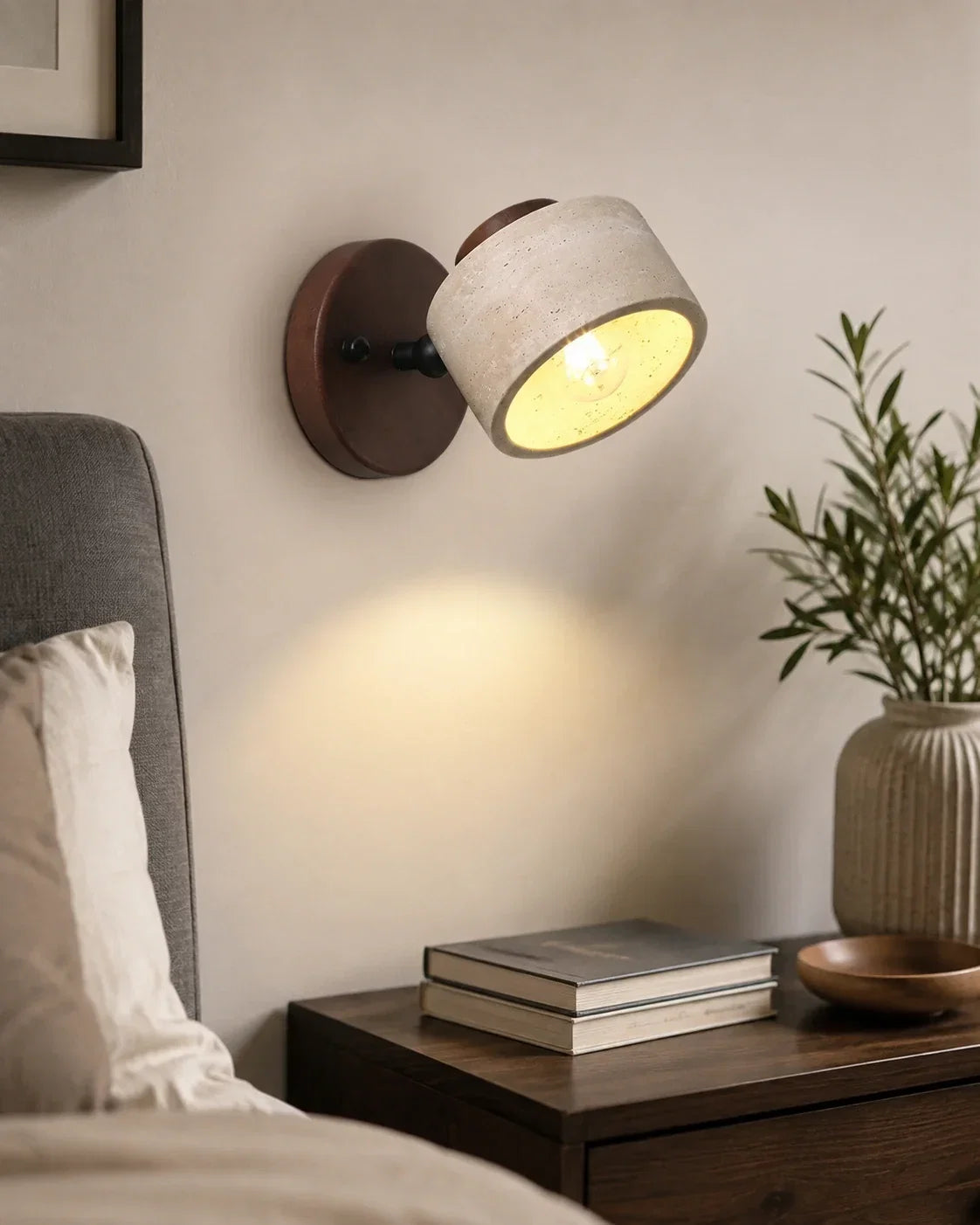 Adjustable wall light featuring a natural travertine spotlight head mounted on a dark wood base, illuminating a bedside table in a Japandi bedroom.
