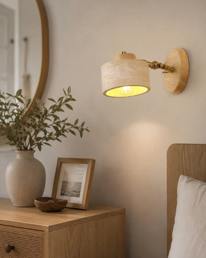 Adjustable wall light featuring a natural travertine shade and wood mount, illuminating a Japandi-style bedroom bedside table with warm, soft light.