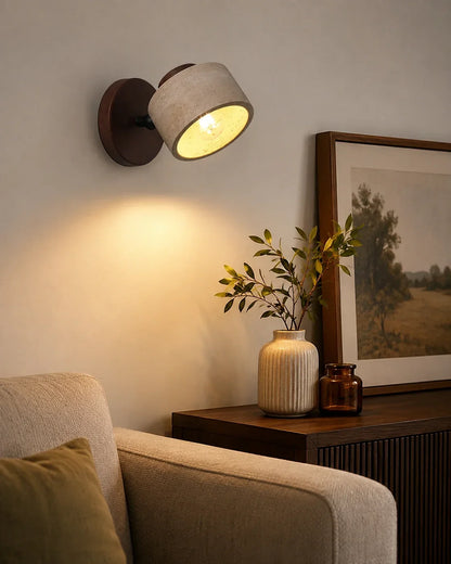 An adjustable travertine and wood wall light casting a warm glow above a wooden sideboard with a vase and framed picture in a cosy room.