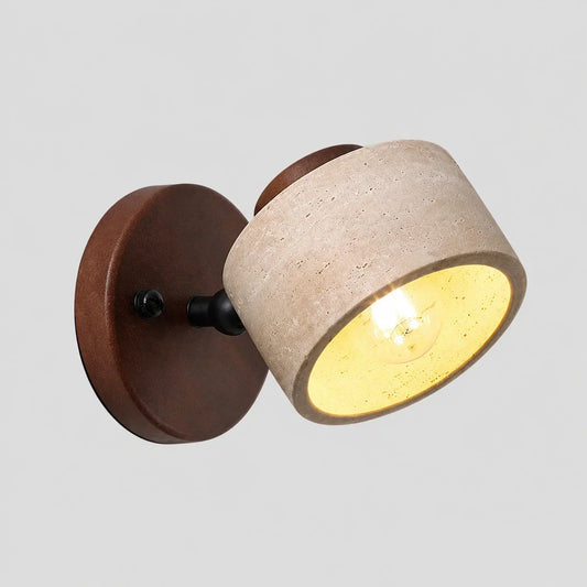 An adjustable wall light featuring a round dark wood base and a cylindrical travertine stone shade, illuminated with a warm glowing bulb.