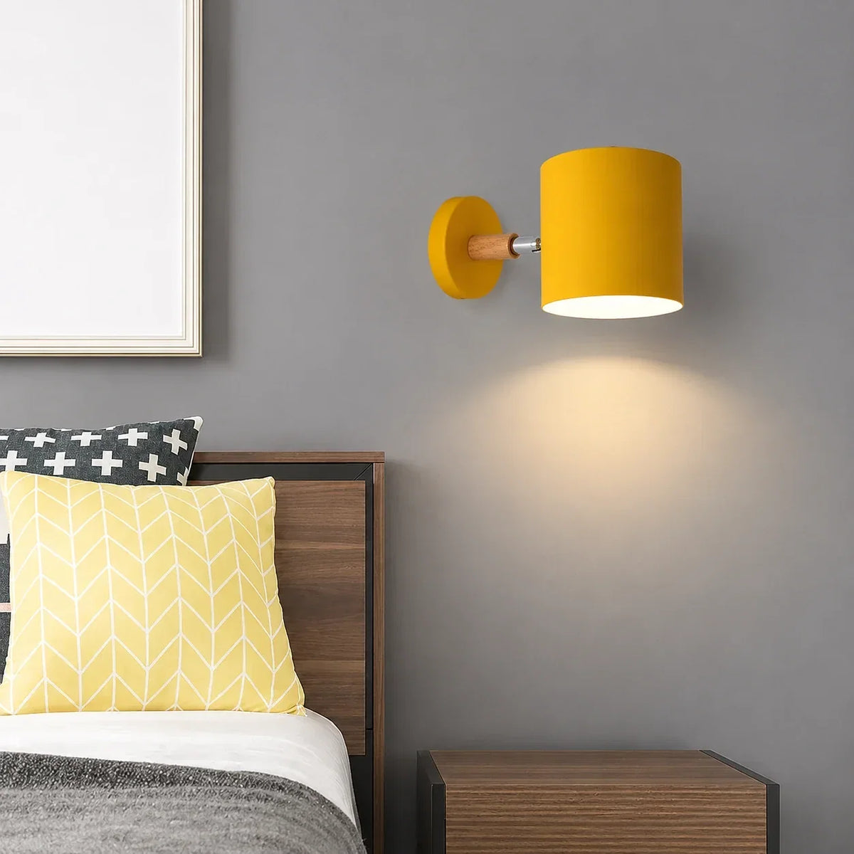 Yellow adjustable wall light with a wood accent mounted on a grey bedroom wall, casting a warm glow above a wooden bedside table.