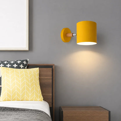 Yellow adjustable wall light with a wood accent mounted on a grey bedroom wall, casting a warm glow above a wooden bedside table.