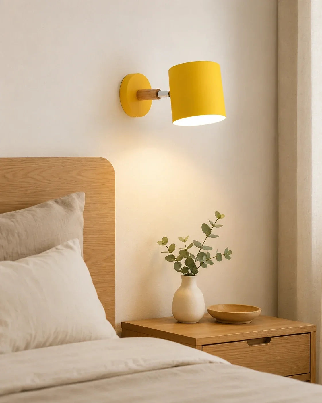 An adjustable yellow wall light with a wood accent mounted above a bedside table in a modern bedroom, casting a warm, cosy glow.