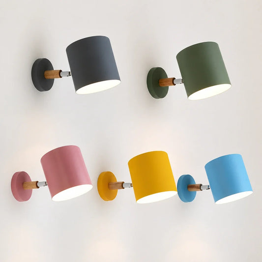 Five adjustable wall lights with wood accents in grey, green, pink, yellow and blue, mounted on a white wall and glowing with warm light.