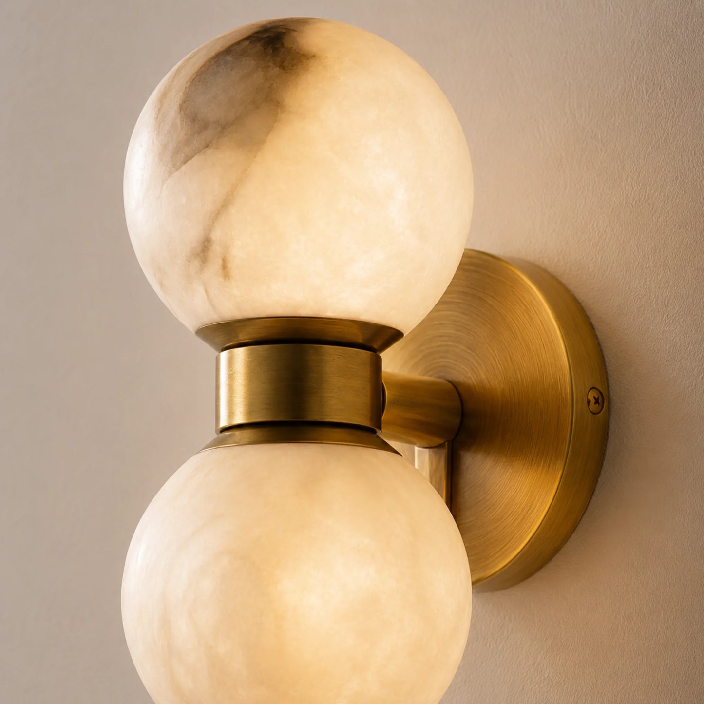 Art Deco wall light featuring two glowing alabaster ball shades mounted on a circular brushed brass base, providing warm ambient indoor lighting.