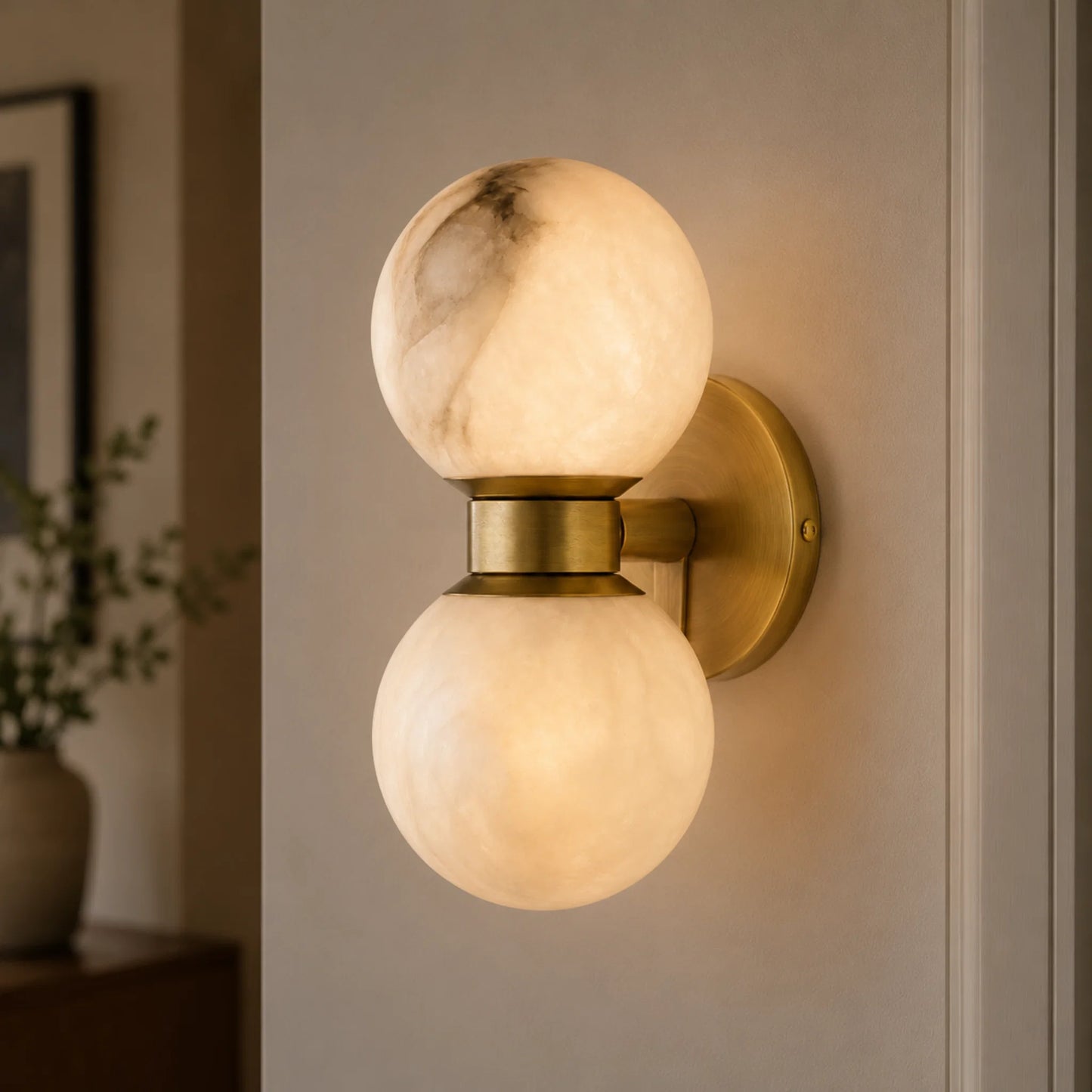 Art Deco wall light featuring two glowing alabaster ball shades mounted on a circular brushed brass base, providing warm ambient indoor lighting.