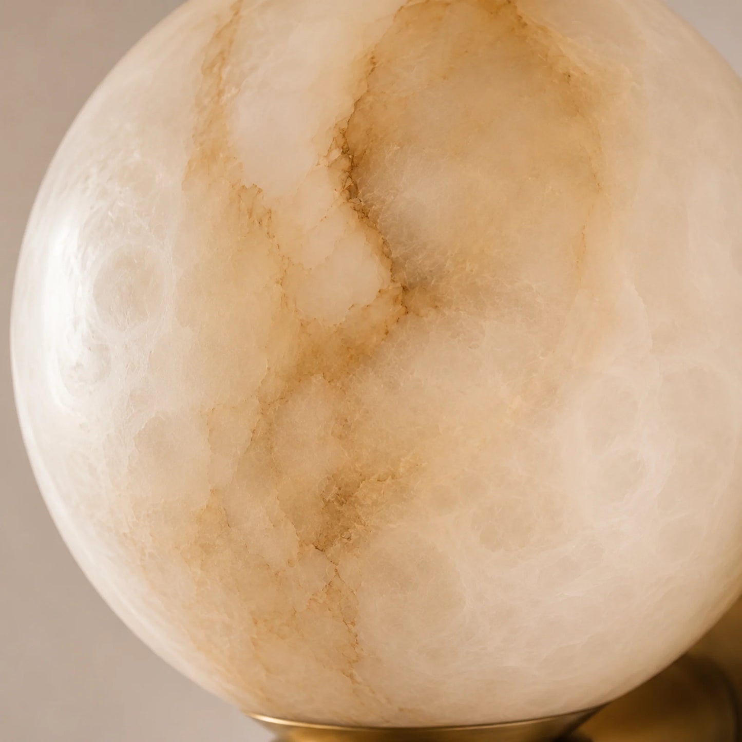 Close-up of a spherical alabaster wall light, showcasing the natural veining and warm, translucent texture of the stone set on a brushed brass base.