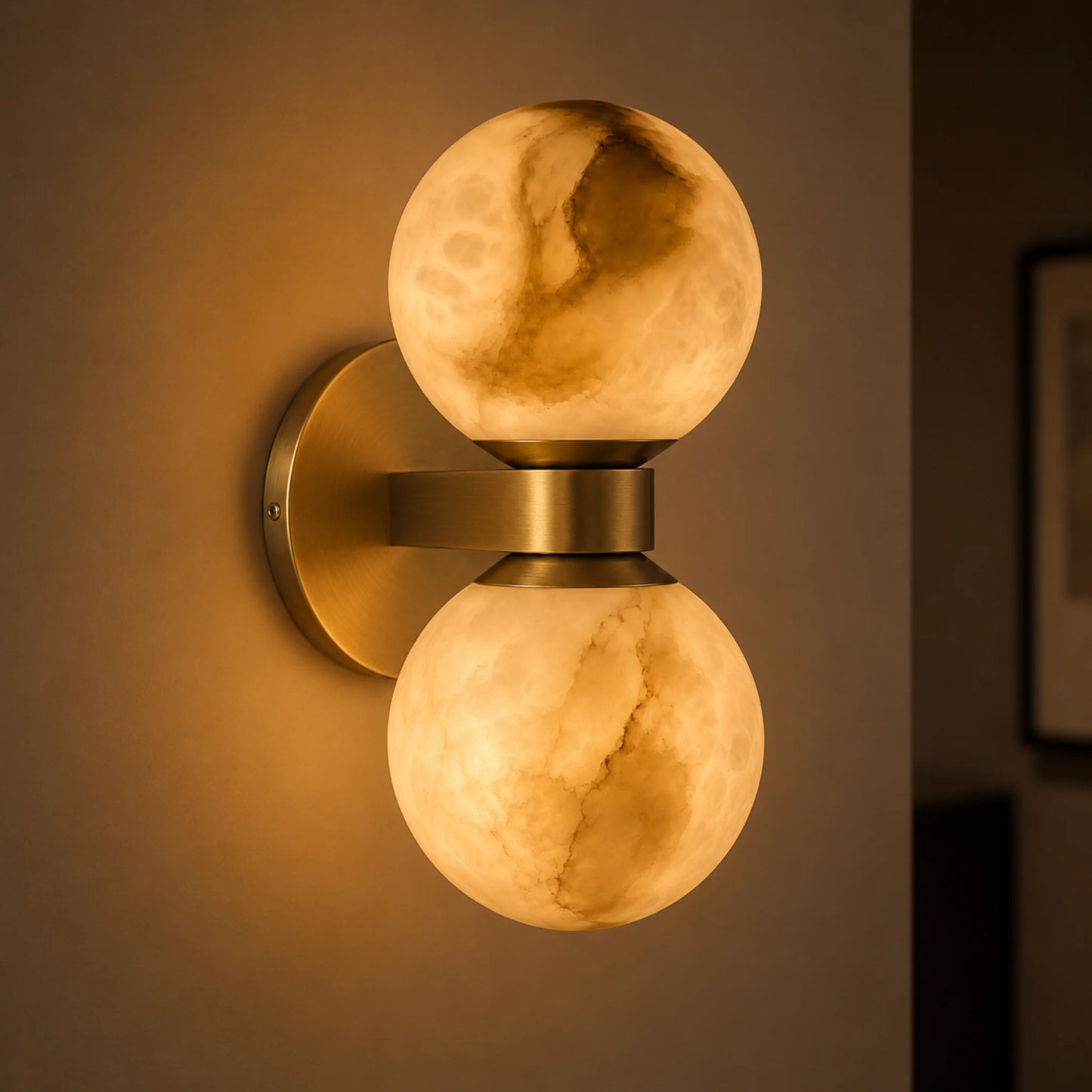 An Art Deco wall light featuring two glowing alabaster balls mounted vertically on a brushed brass base, emitting a warm, ambient light.