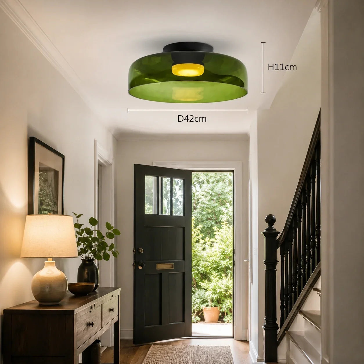 An Art Deco green glass flush ceiling light with a warm yellow glow, mounted in a home hallway. Dimensions of H11cm and D42cm are indicated.