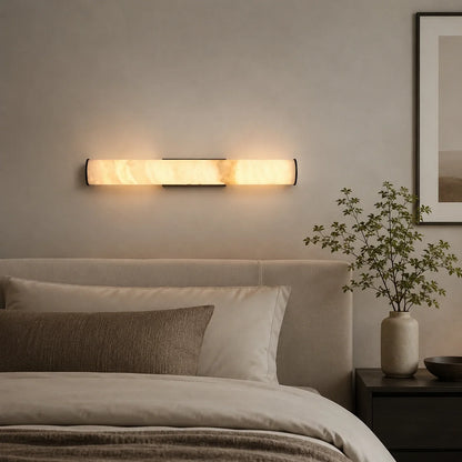 An Art Deco LED wall light with a glowing simulated marble shade mounted on a neutral wall above a bed in a modern, minimalist bedroom.