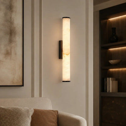 Art Deco LED wall light with a glowing, cylindrical simulated marble shade, mounted vertically on a neutral wall in a modern living room.