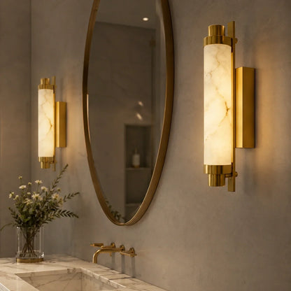 Two Art Deco LED wall lights with gold-coloured fixtures and glowing simulated marble shades, mounted on a grey wall beside an oval mirror.