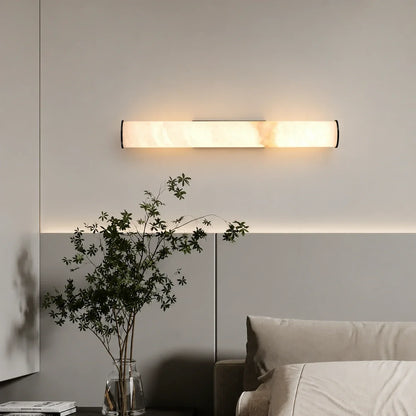 An elegant horizontal Art Deco LED wall light with a simulated marble shade, emitting a warm glow above a bed in a modern bedroom.