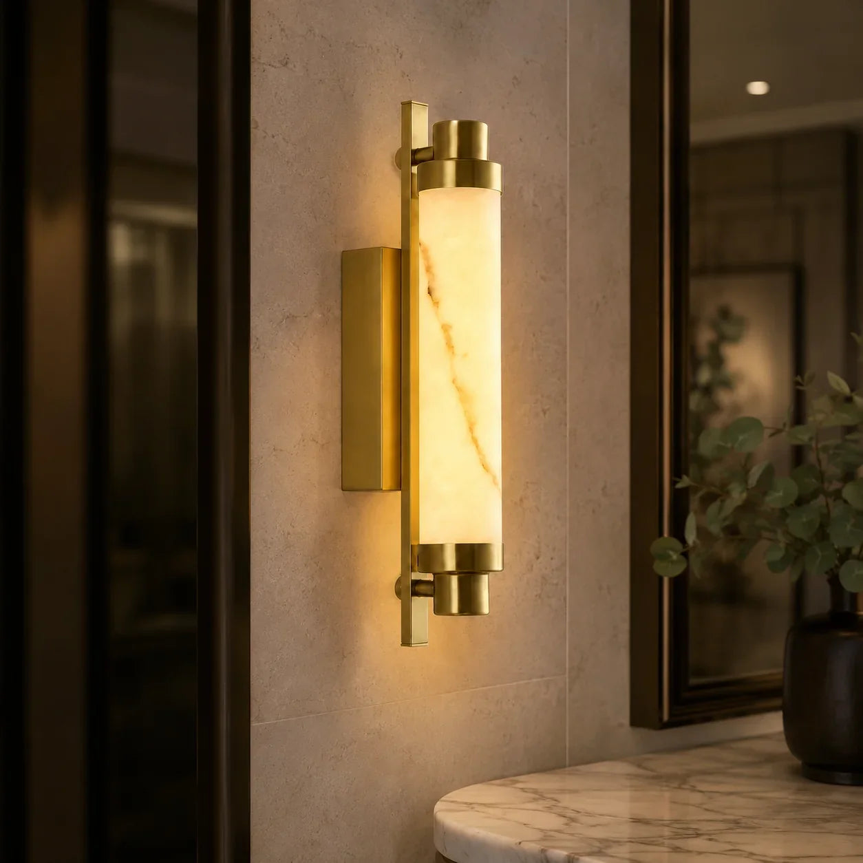 An Art Deco LED wall light with a gold-finished frame and a glowing warm white marble-effect cylindrical shade, mounted on a tiled wall.