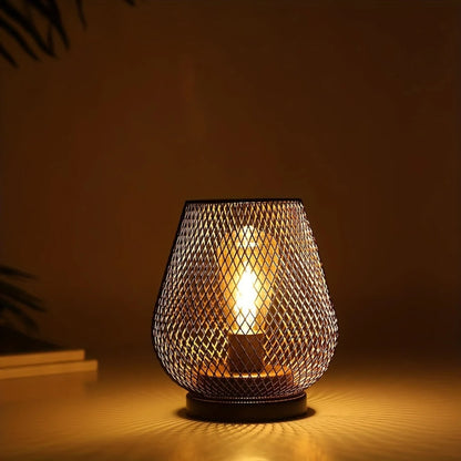 Battery operated table lamp with a black metal mesh shade casting a warm, ambient glow onto a surface, perfect for industrial style home decor.