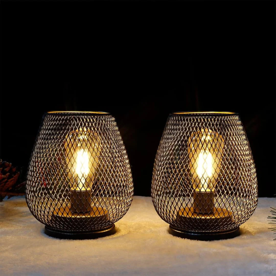 Two battery-operated LED table lamps with a black metal mesh design, emitting a warm glow on a white surface against a dark background for ambient lighting