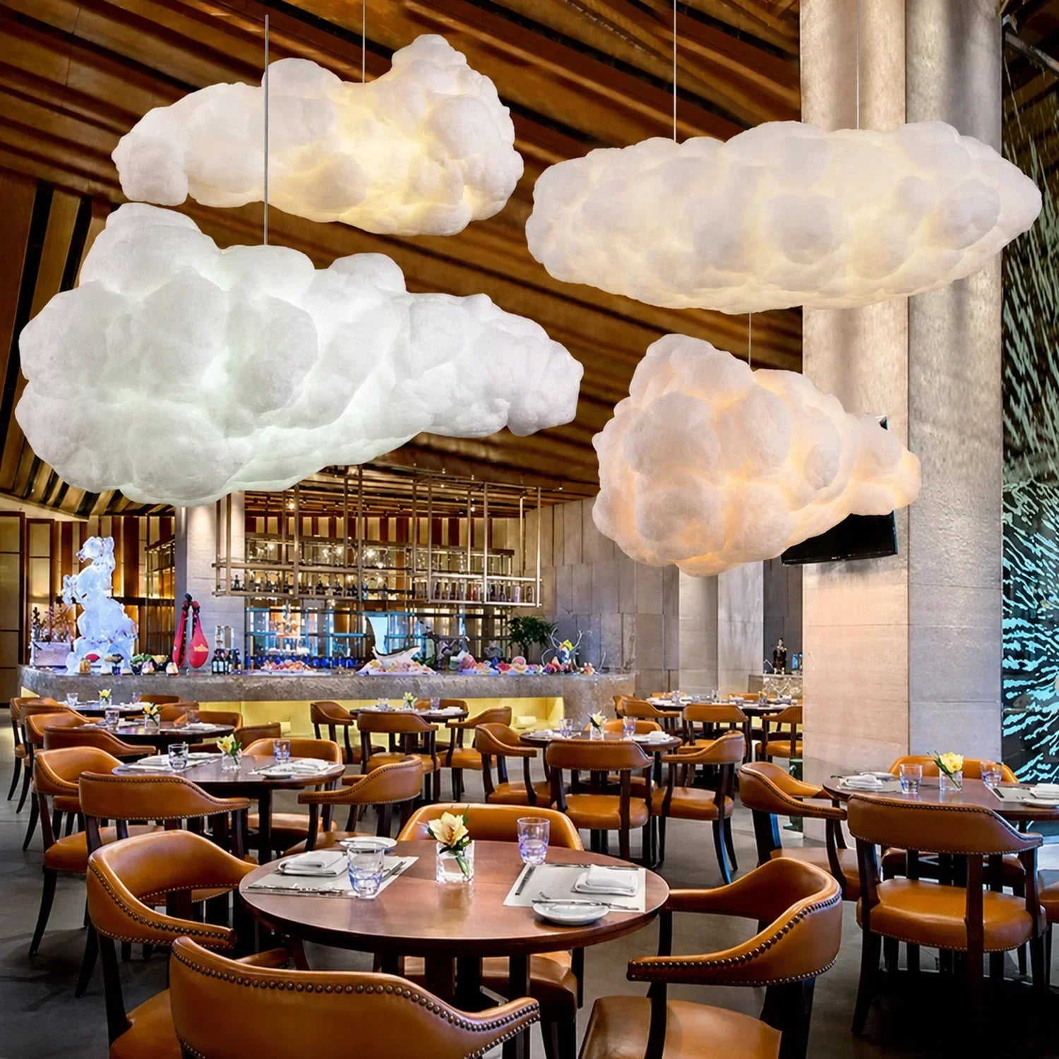 Three sculptural cloud pendant lights suspended above tables in a modern restaurant interior with warm lighting and leather chairs.