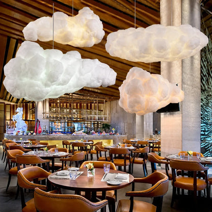 Three sculptural cloud pendant lights suspended above tables in a modern restaurant interior with warm lighting and leather chairs.