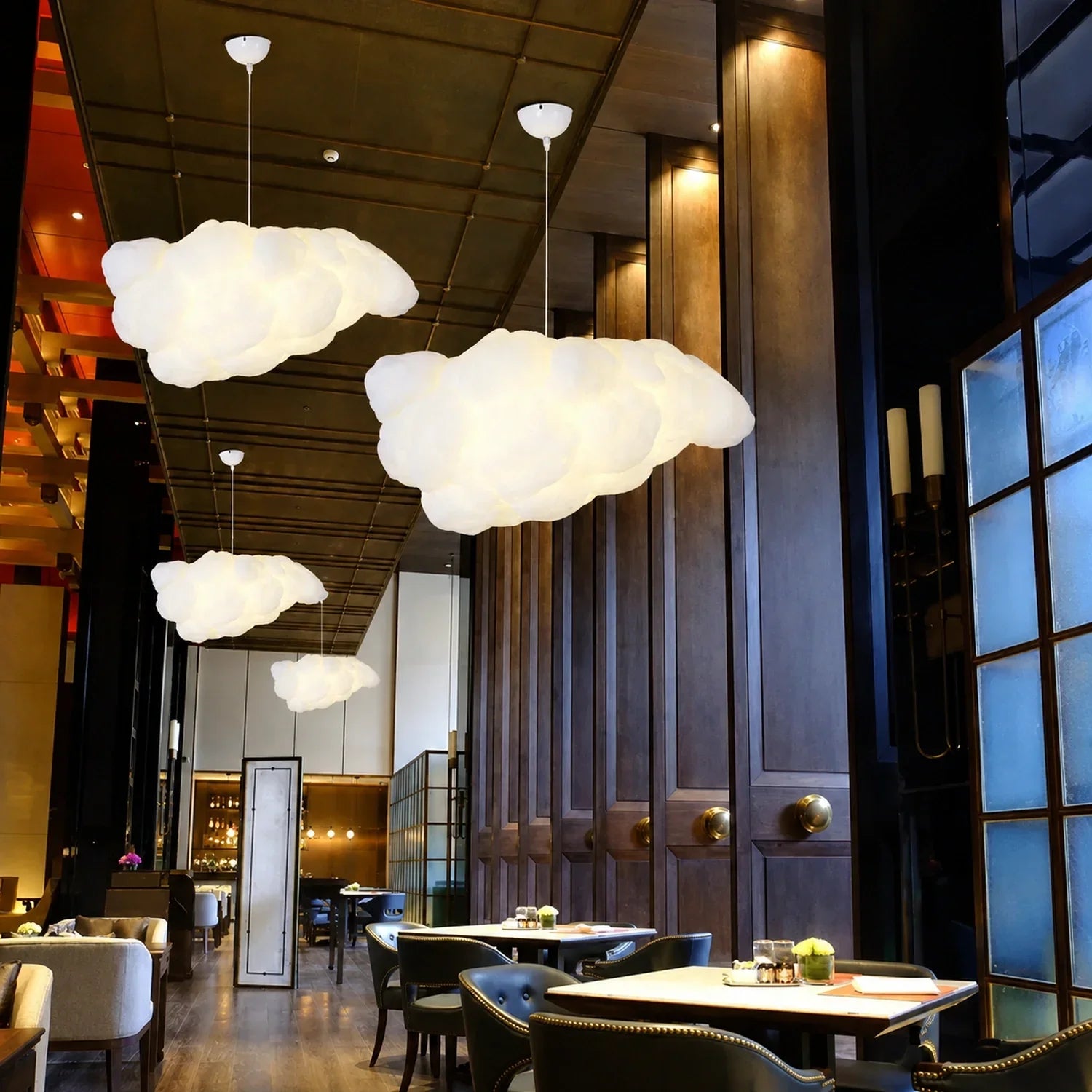 Multiple sculptural cloud pendant lights hanging in a modern, dark-toned restaurant interior, creating a soft, ambient glow above dining tables.