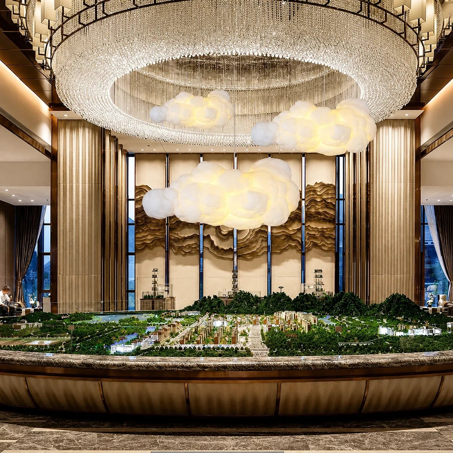 Three sculptural cloud pendant lights suspended beneath a large crystal chandelier in a luxurious interior space featuring a detailed architectural model.