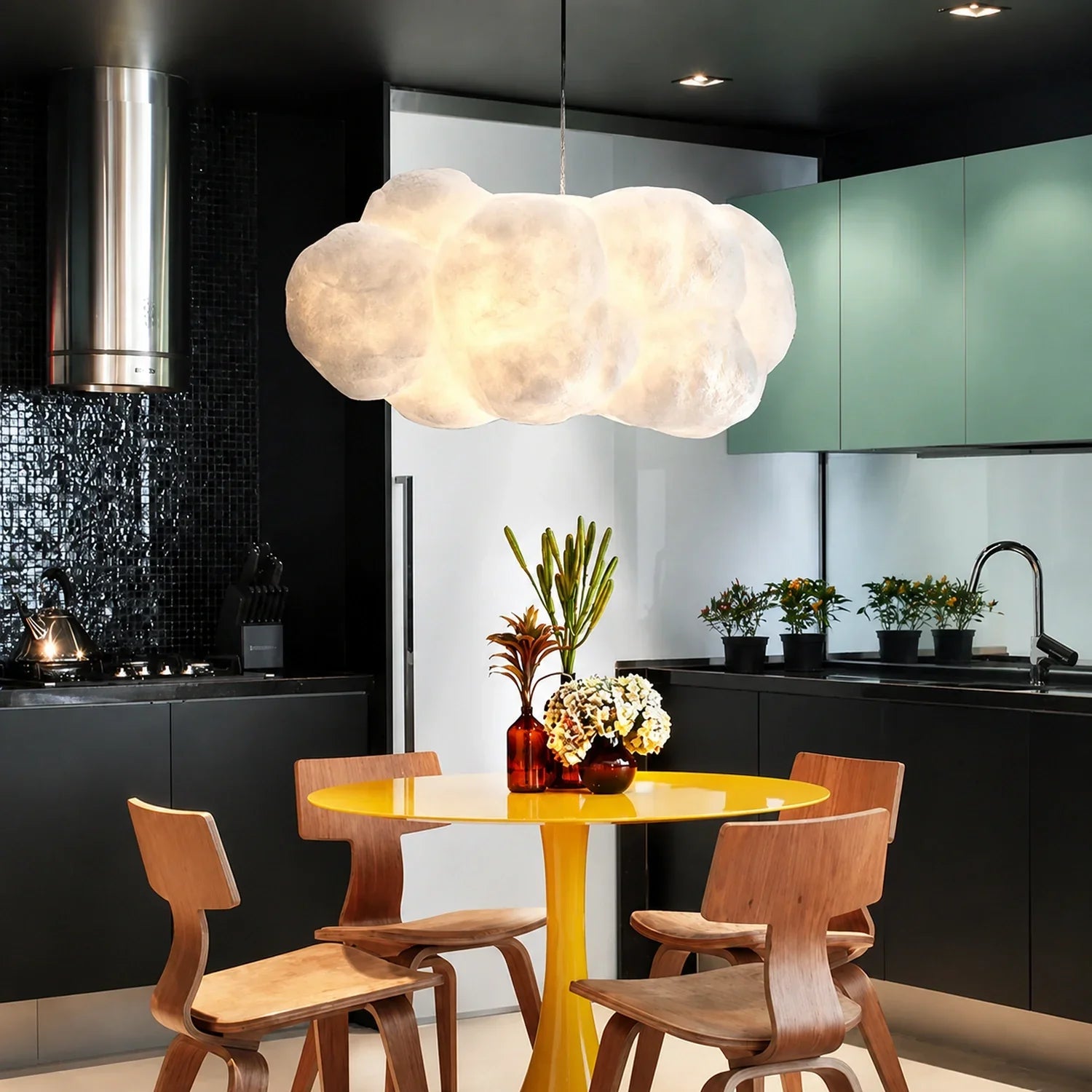 A sculptural cloud pendant light hangs above a bright yellow circular dining table with wooden chairs in a modern kitchen with black cabinetry.