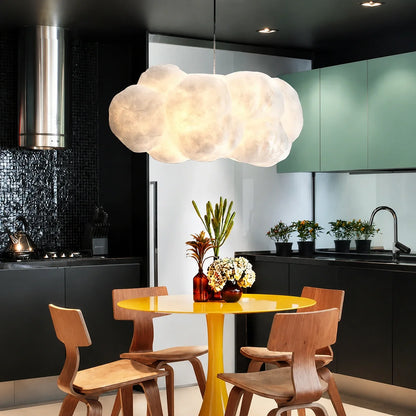 A sculptural cloud pendant light hangs above a bright yellow circular dining table with wooden chairs in a modern kitchen with black cabinetry.