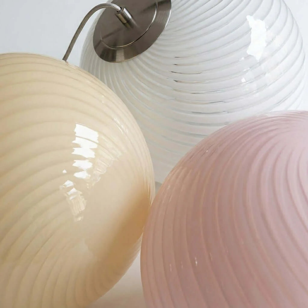 Three spherical pendant lights with a modern swirl glass design in cream, white, and soft pink, featuring brushed metal ceiling fittings.