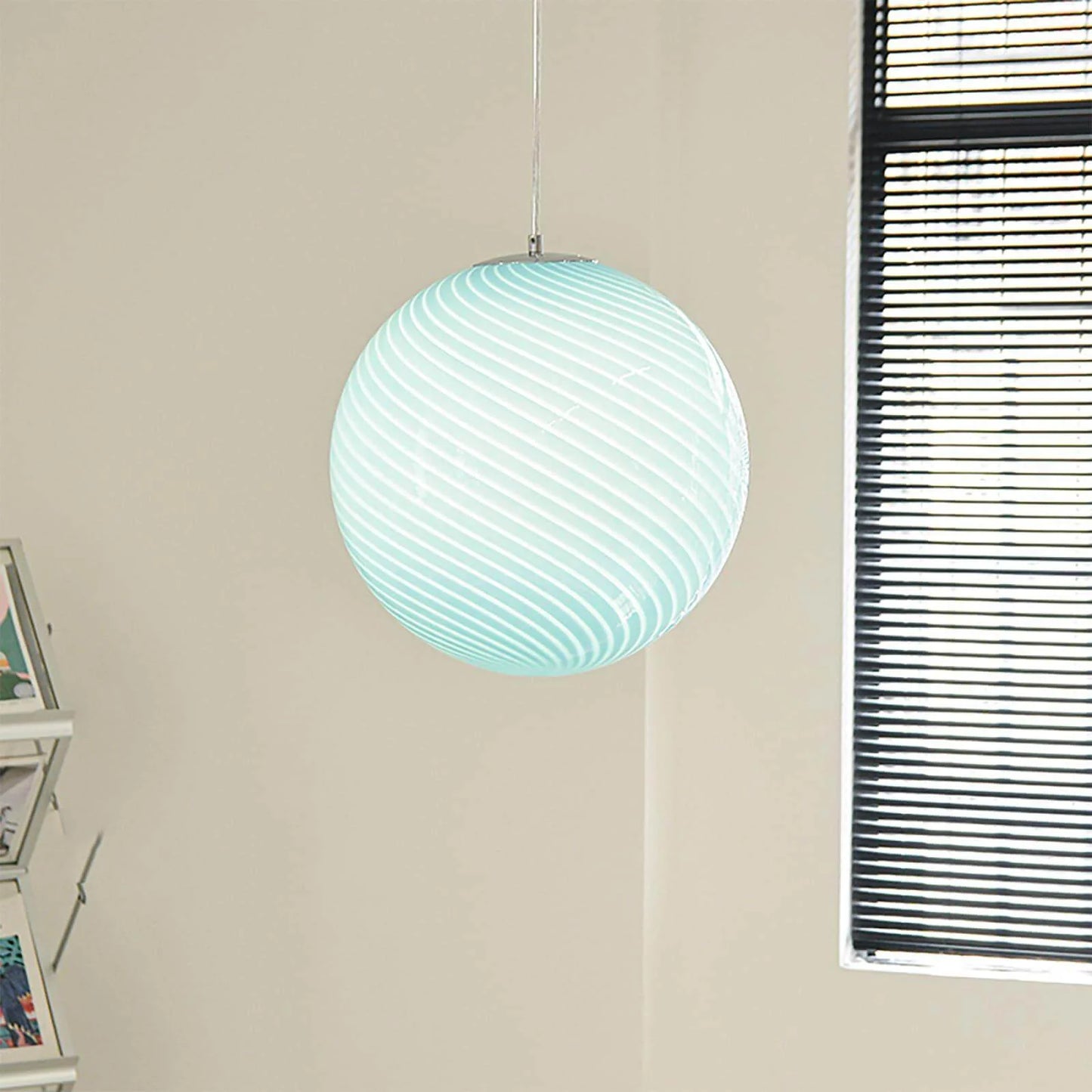 A modern spherical pendant light with a pale blue and white swirl glass design, suspended from a simple chrome fitting in a bright, neutral room.