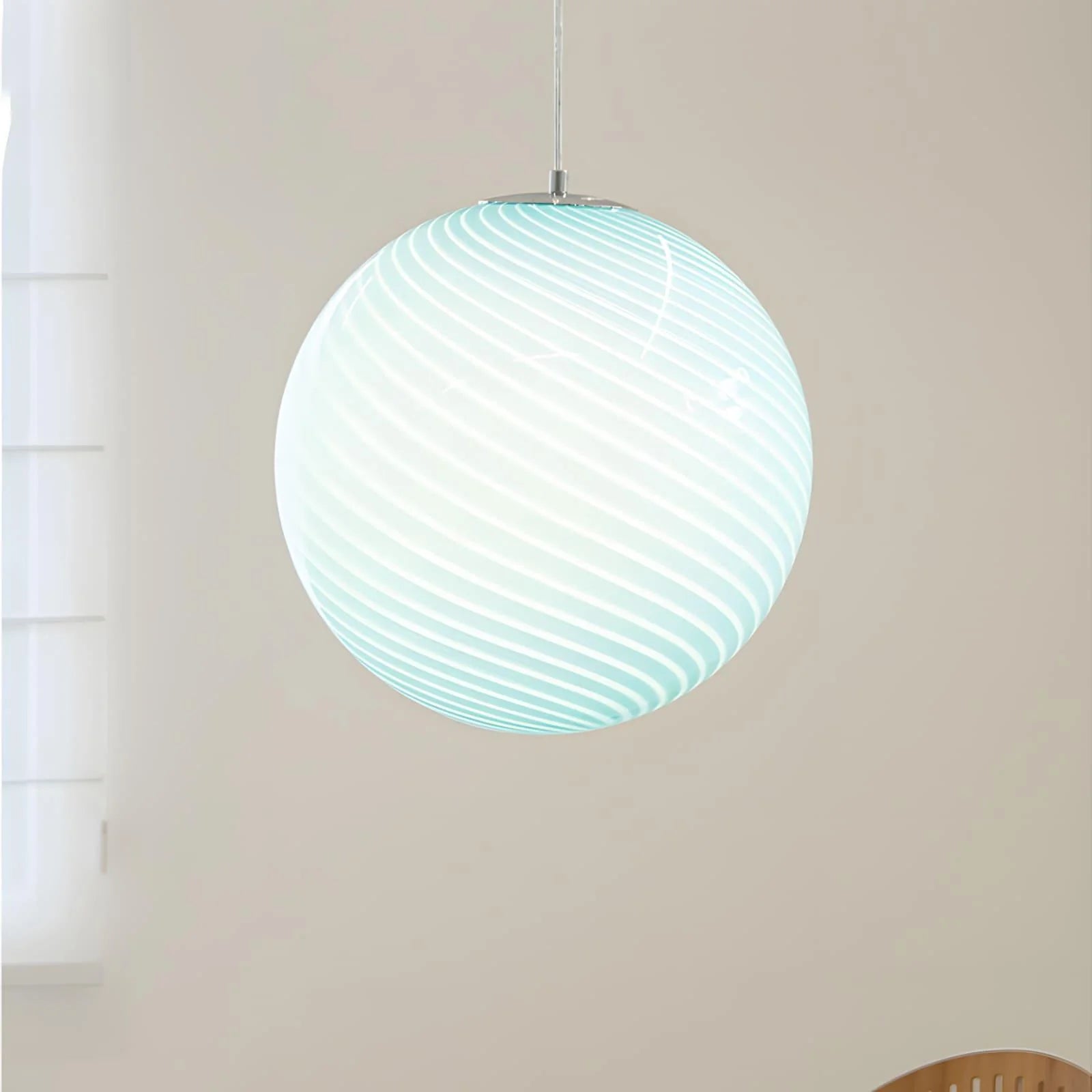 A modern spherical pendant light featuring a decorative pale blue and white swirl glass shade, suspended by a simple metal fixture in a bright room.
