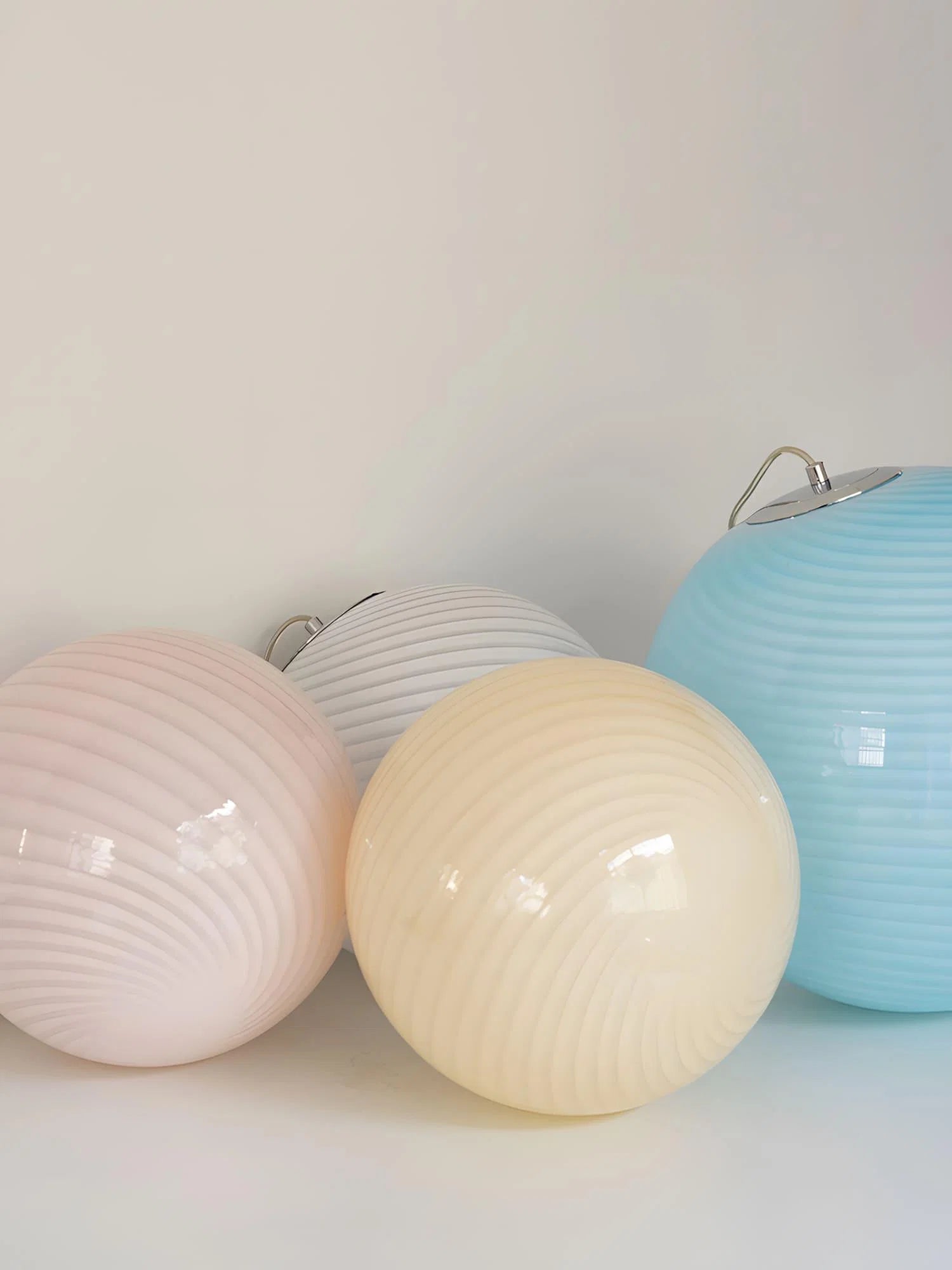 Four spherical pendant lights with a colourful swirl glass design in pastel shades of pink, white, cream and blue, arranged on a white surface.