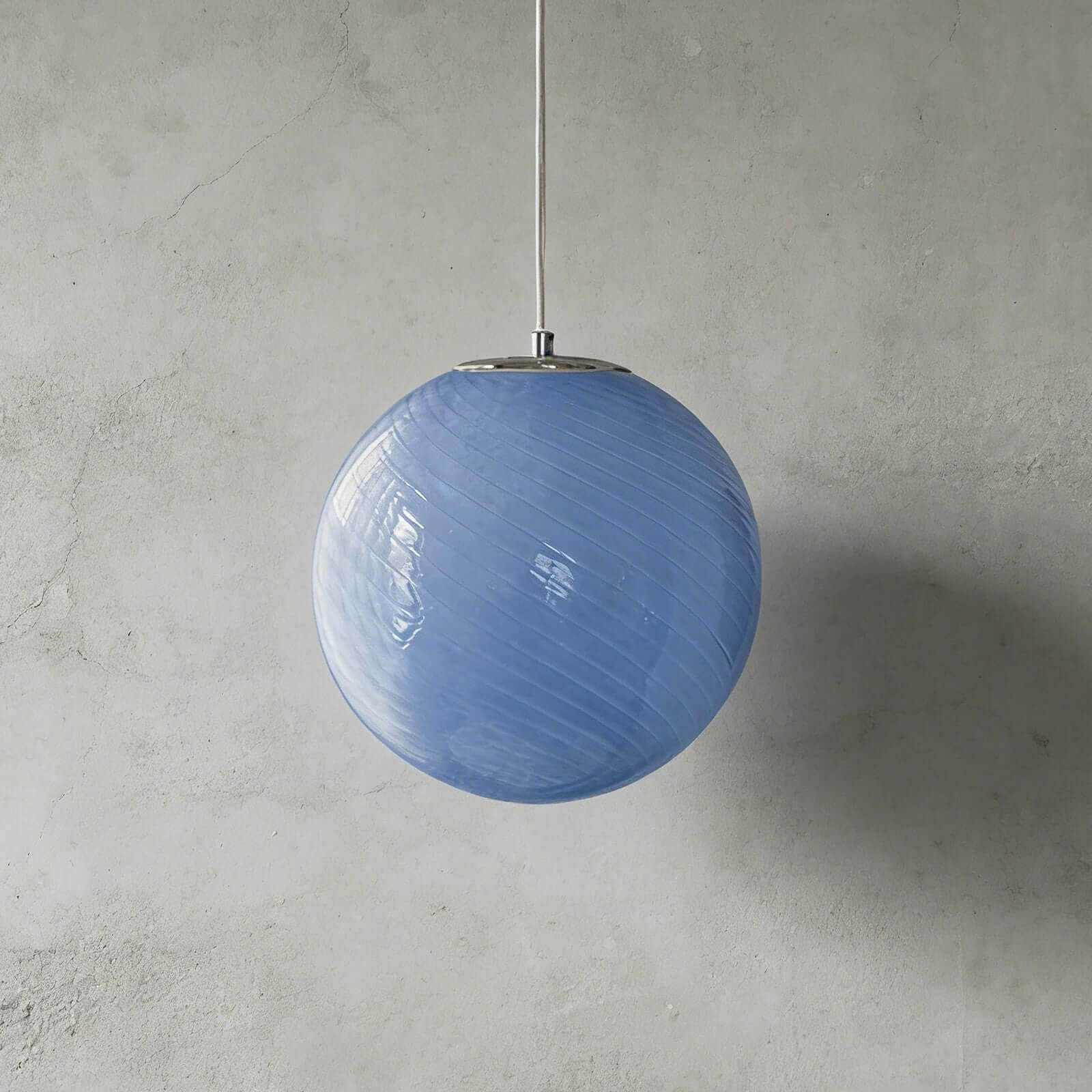 A modern spherical pendant light featuring a blue glass shade with a subtle swirl pattern, suspended by a simple cord against a grey concrete wall.