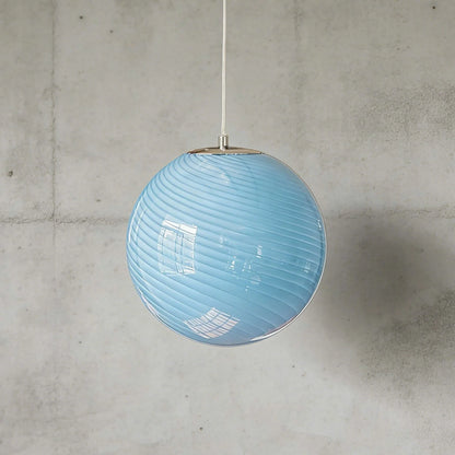 A modern spherical pendant light featuring a light blue glass shade with a subtle white swirl pattern, suspended against a grey concrete wall.