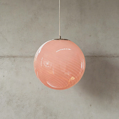 A modern spherical pendant light featuring a soft pink glass shade with a subtle swirl pattern, suspended against a neutral grey concrete wall.