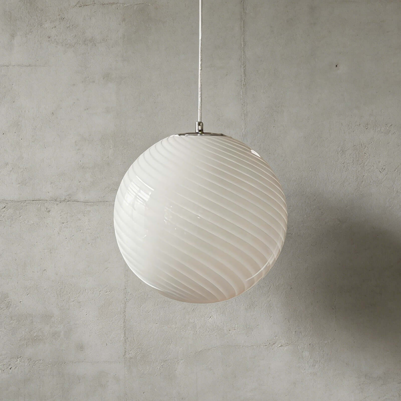 A modern spherical pendant light with a white glass shade featuring a subtle swirling pattern, suspended against a textured grey concrete wall background.